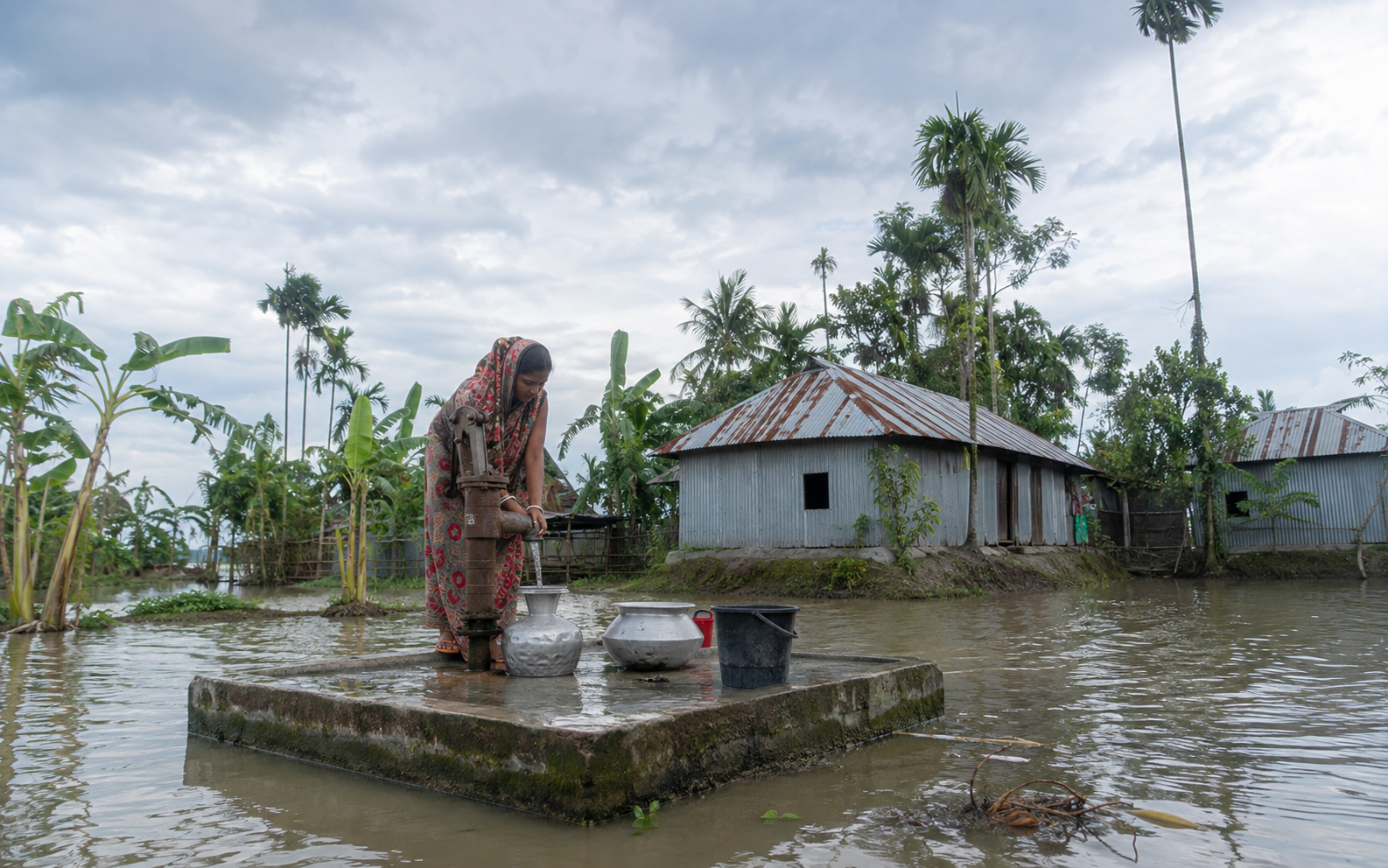 A woman collecting water from a raised tube well during flooding.